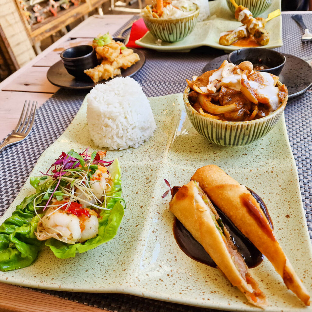 Royal squid lunch tapas with Crispy spring rolls with duck and plum sauce, samui zingy prawns with spicy sauce and spring onions, lamb massaman curry and jasmine rice served on a pale green plate