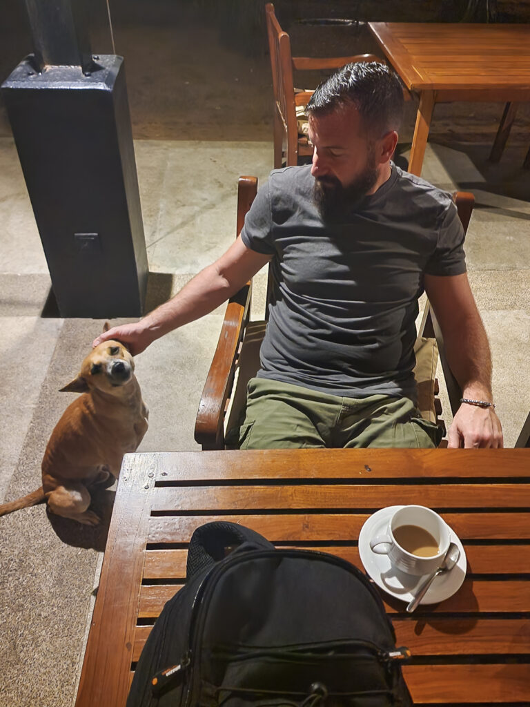Luke stroking a dog and drinking a cup of coffee