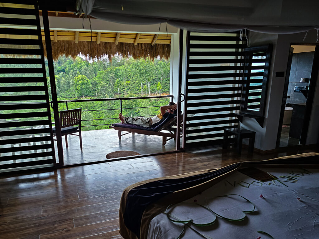 Luke sitting on a sun lounger on a balcony looking over the tea plantations at 98 Acres Resort and Spa Hotel