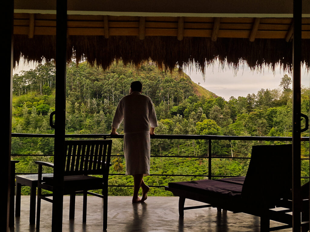 Luke standing in his robe on the room balcony looking over the Little Adams Peak and the tea plantations in Ella Sri Lanka