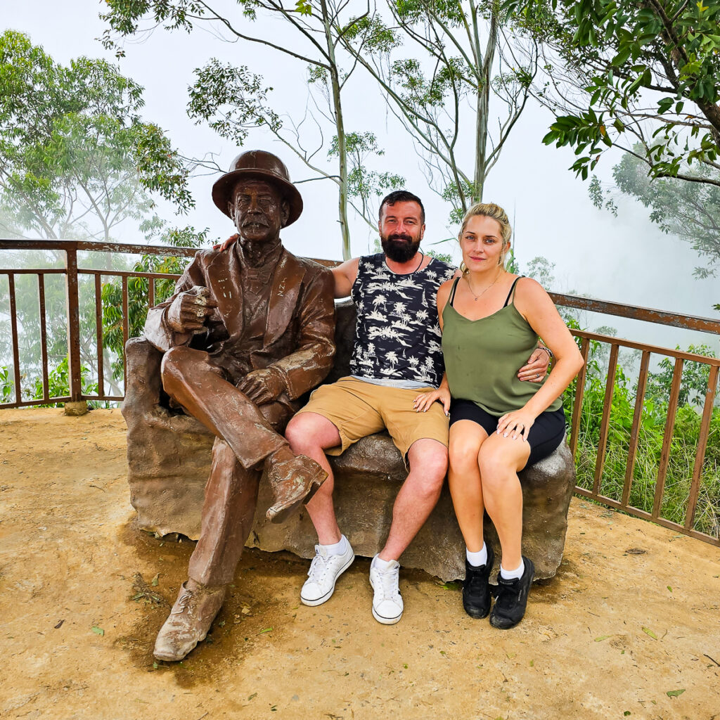 Luke and Kay sitting next to a statue of Sir Thomas Lipton at the highest view point of Lipton tea plantation in Ella Sri Lanka