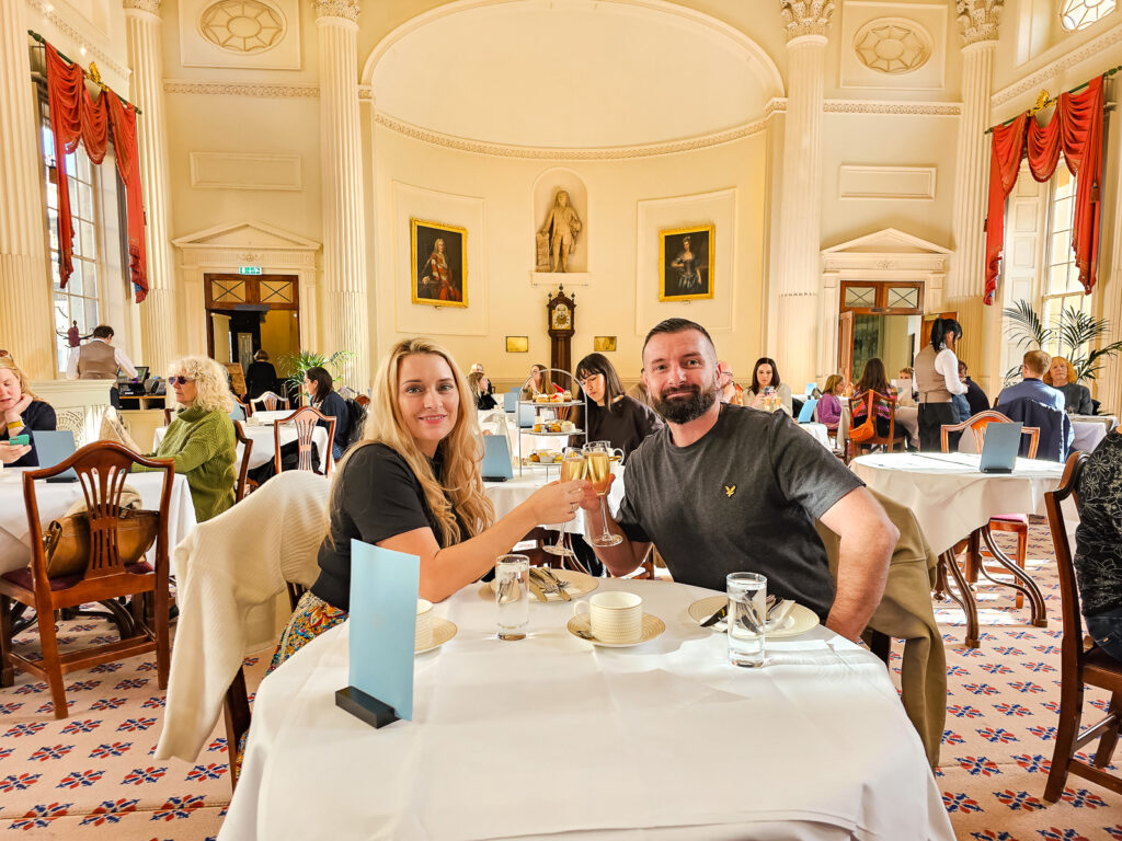 Luke and Kay holding a glass of prosecco each sitting at the table in the restaurant in the pump room in bath