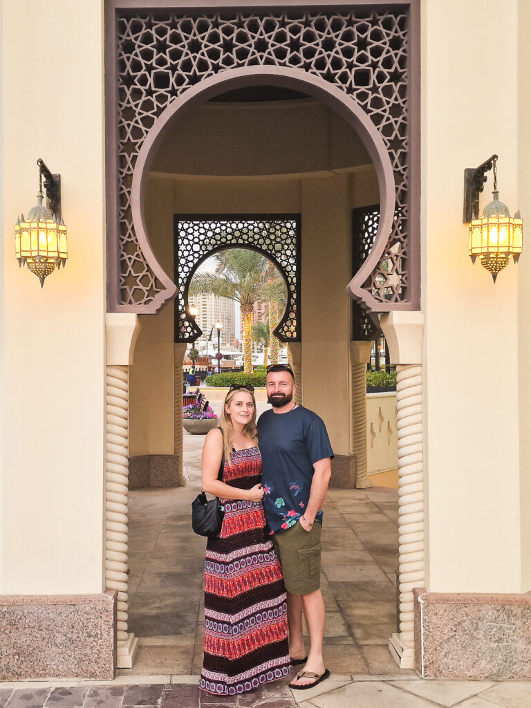 Luke and Kay from Flawless Journeys standing under an Arabic arch building at the marina in the The Pearl Qatar Doha