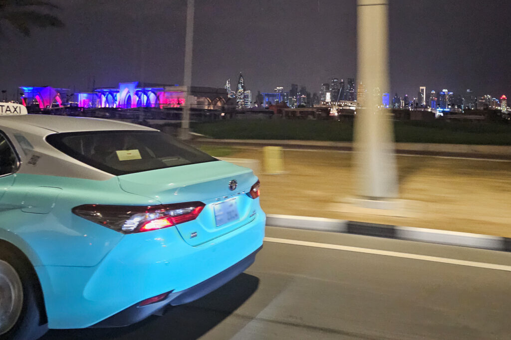 Aqua blue taxi driving on the roads in Doha Qatar with the West Bay Skyline in the background
